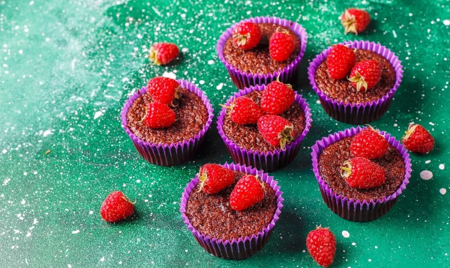 4 petits muffins dorés aux framboises fraîches dans leurs ramequins, micro-ondes en arrière-plan
