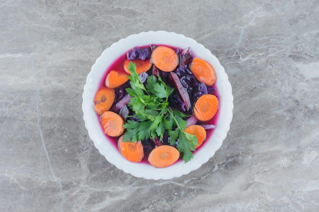 Salade colorée de carottes râpées et betteraves cuites dans un bol blanc, garnie d'herbes fraîches sur fond clair